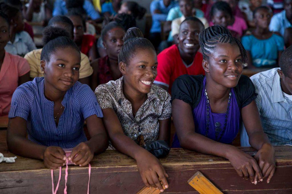 Three young women sitting together at a wooden table smile during a GADES workshop.