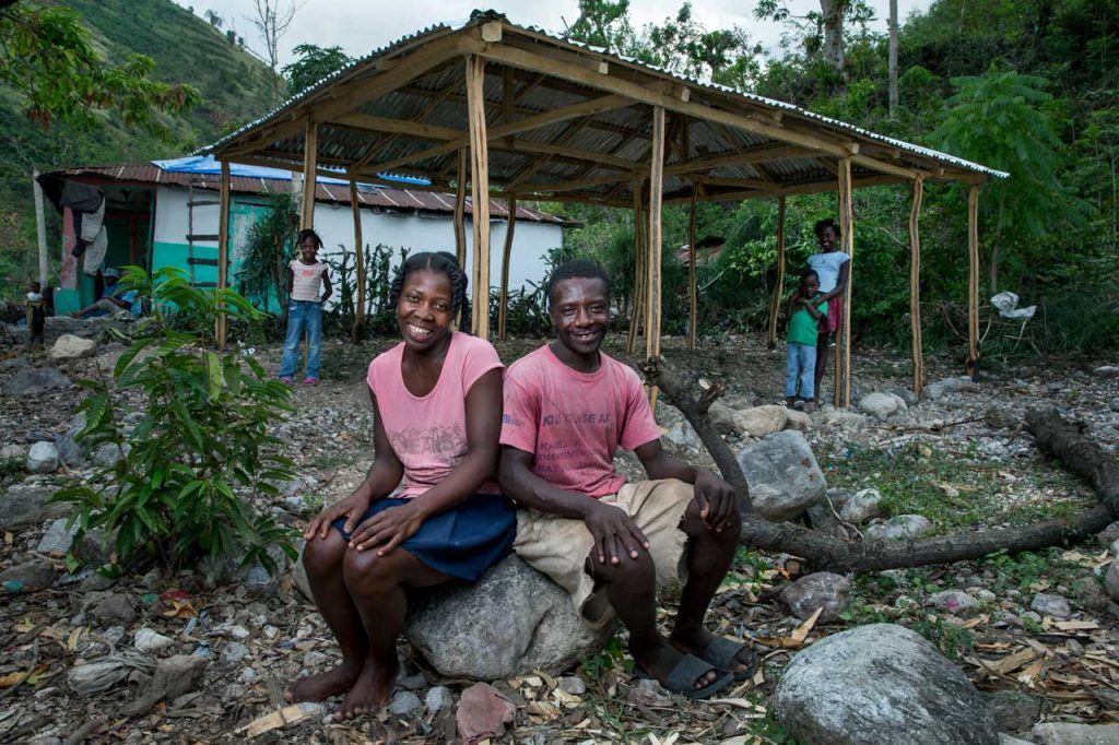 Perlage St.-Rose and Nico Aseau sit outside on some rocks near their home with a new tin roof, thanks to BDHH.