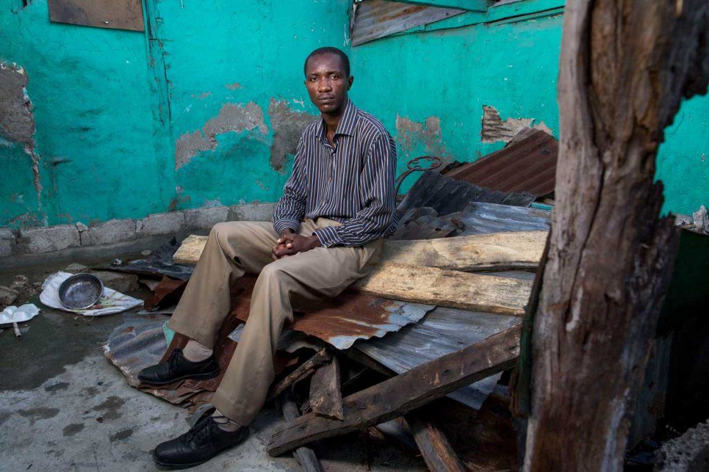 Vernace Denis sits on top of the fallen roof inside of his home that was damaged by Hurricane Matthew in Les Cayes.