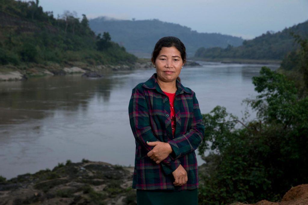 Ja Hkawn standing with her arms crossed on the bank of the Irawaddy River, near the proposed site of the Myitsone Dam