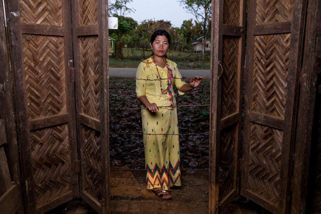 Ja Hkawn holding the barbed wire strung across the door at the site of her old home and store, which she was forced to abandon and is now in ruins.