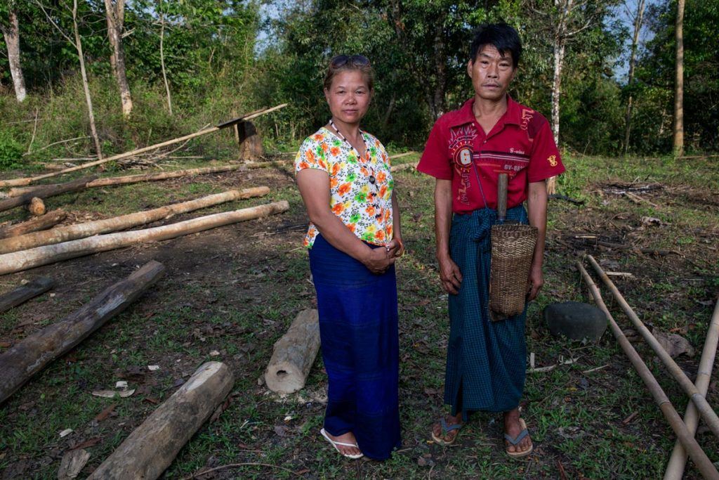 Lu Ra and her husband stand in a clearing at the site of their old home in their old village, where they are hoping to move back.