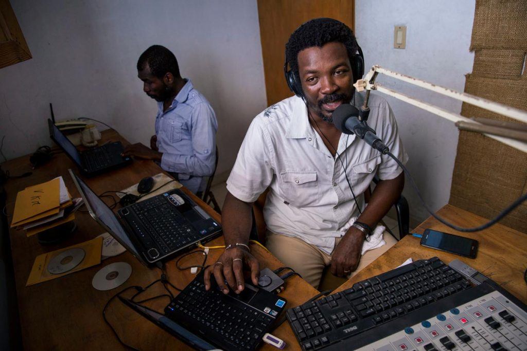 Radyo VKM’s Max-Imbert Marcelin (speaking into a radio microphone) and Claude Charles (sitting at a laptop in the back) are using the airwaves to support recovery efforts in Haiti’s Southern Department following Hurricane Matthew. Photo by Jonathan Torgovnik