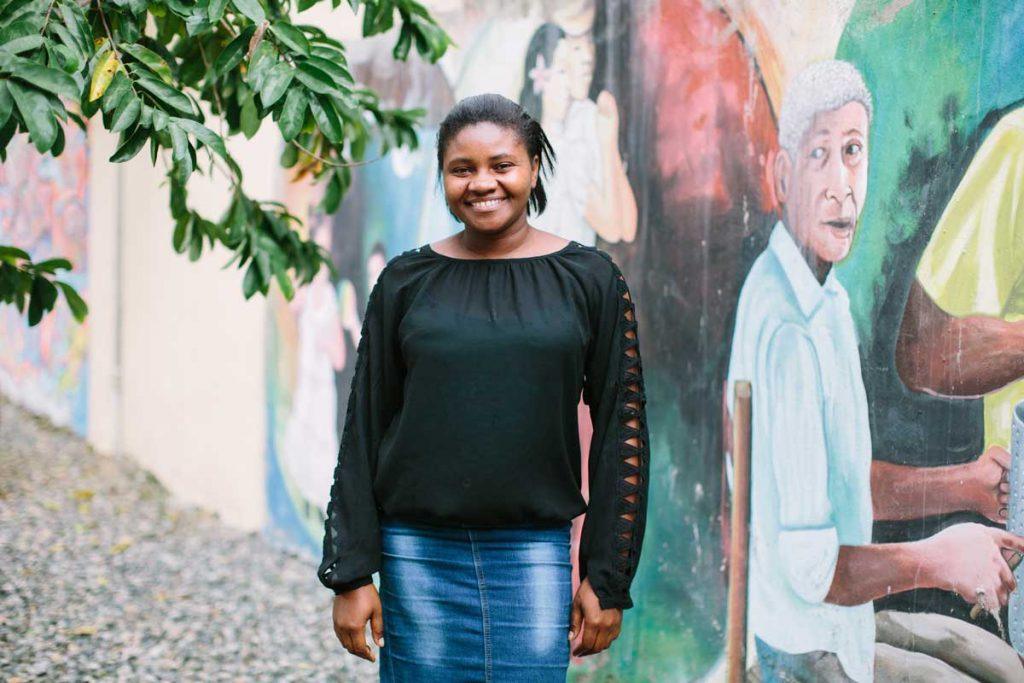 Rosanny Romilis standing in front of a colorful mural outside, smiling at the camera.