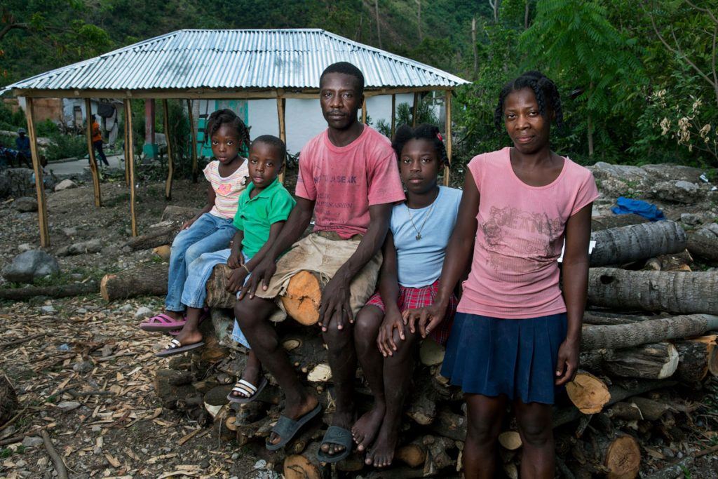 After Hurricane Matthew, AJWS grantee BDHH helped Nico and Perlage and their three children rebuild their home in the remote community Gwo Woch, on Haiti’s southern peninsula. Here, the family members look at the camera with somber expressions while sitting on a pile of downed trees, near their new home with a tin roof. Photo by Jonathan Torgovnik