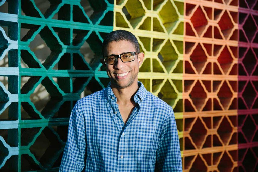 RevASA volunteer Deivis Ventura, wearing glasses and smiling in front of a colorful wall at the group’s Santo Domingo office. Photograph by Christine Han