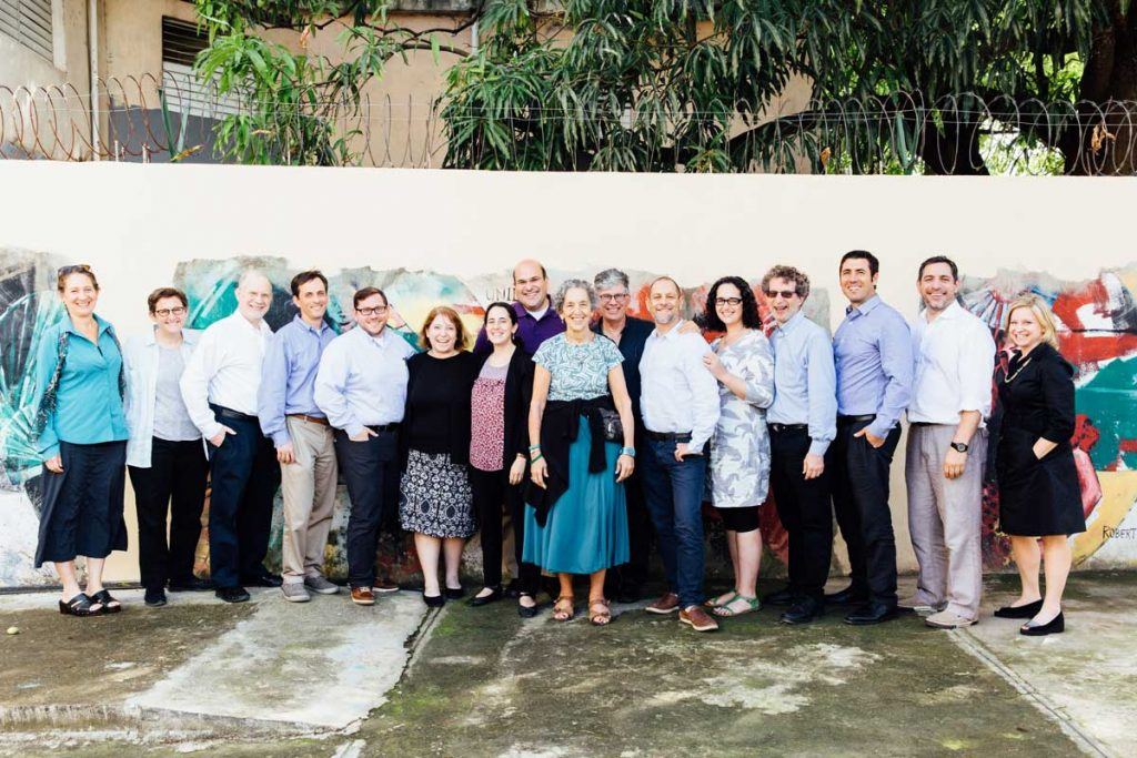 The 15 Global Justice Fellows standing in front of a wall with a mural. AJWS Global Ambassador Ruth Messinger is front and center. The rabbis and cantors are smiling. Photo by Christine Han Photography. 