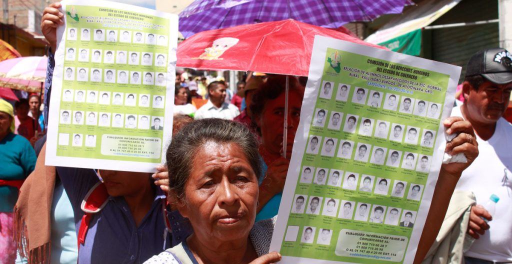 A woman holding a sign with photos of the 43 missing students.