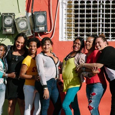 group of women standing outside in front of an orange building, smiling at camera