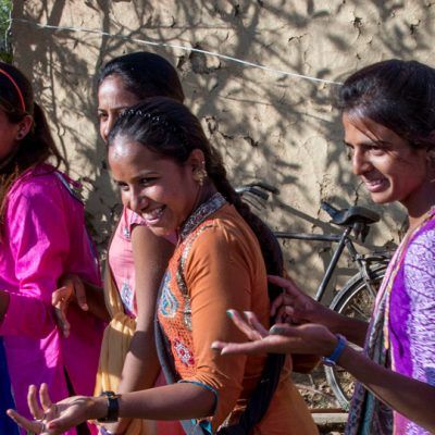 girls in the sunshine, looking at something off camera and smiling. they are wearing purple, orange, and pink dresses