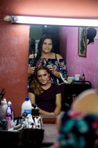 Members of Estrellas participate in a cosmetology vocational training, with one person doing another person's hair, both of them looking in the mirror. Photo by Jonathan Torgovnik