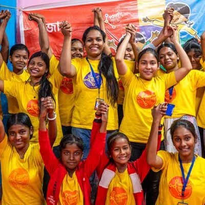 group of celebrating young people wearing matching yellow tshirts, their hands in the air, smiling