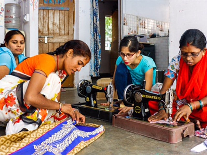 four women working on sewing projects, using two sewing machines