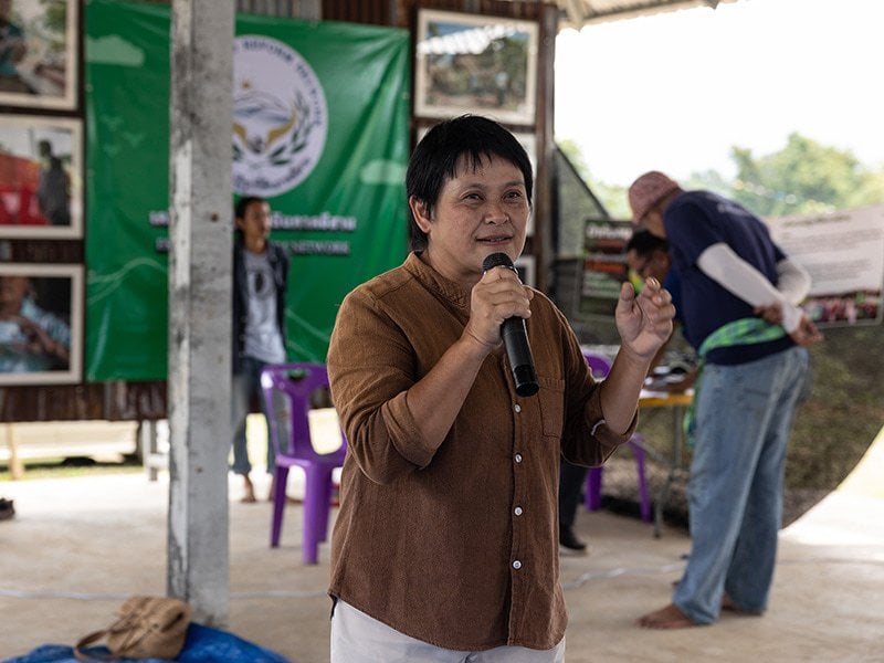 person speaking into microphone outside, wearing a brown button down shirt