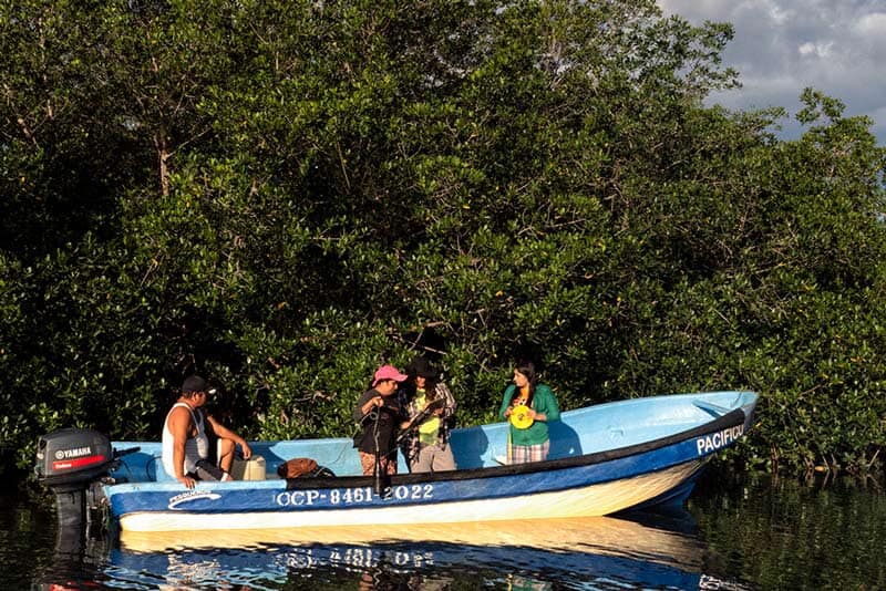 a few people in a canoe on a lake with greenery behind them