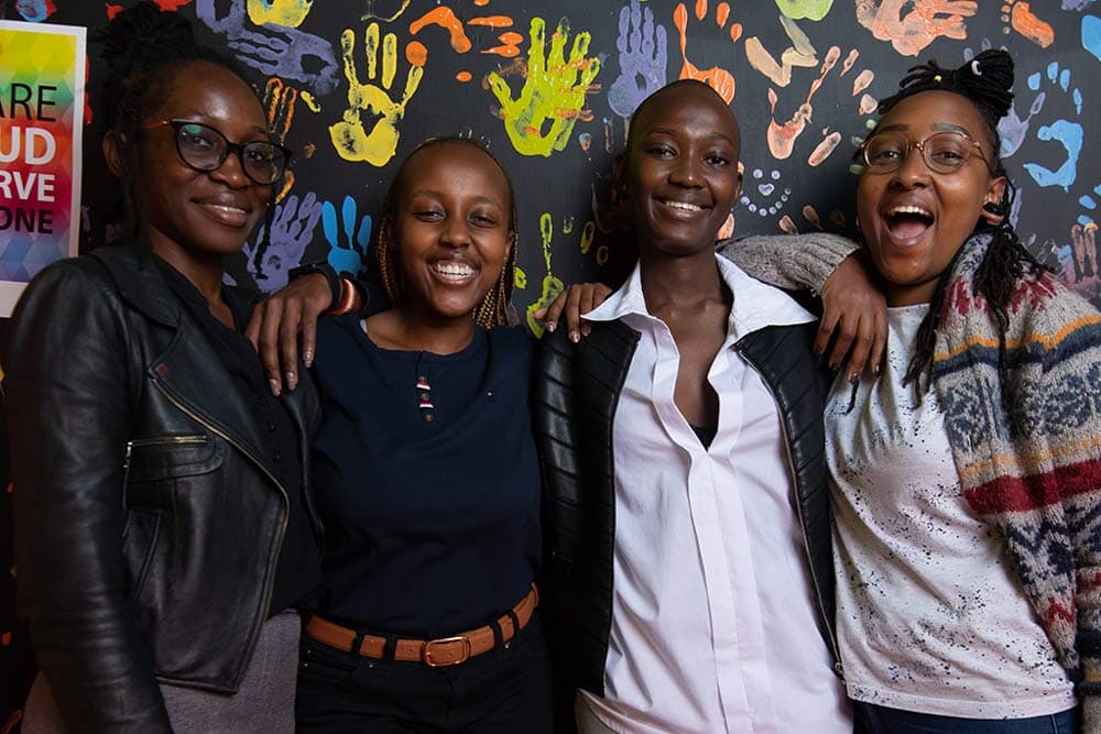 group of young people smiling at camera with wall of painted handprints behind them
