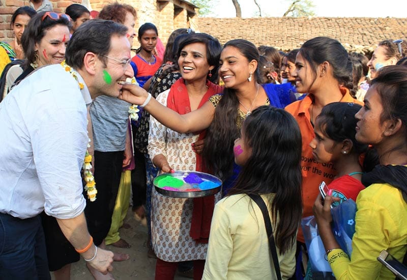 group of women smiling and applying colorful face powder onto a man smiling back at them