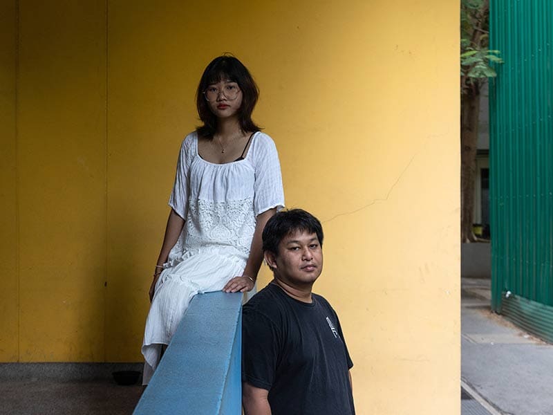 two people with yellow wall behind them, looking at camera