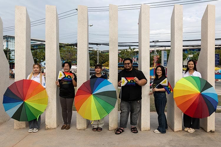 group of people outside holding rainbow pride flags and umbrellas