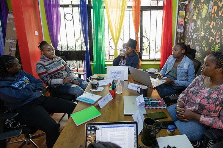 group of people around a table, with a window and rainbow curtains in the background