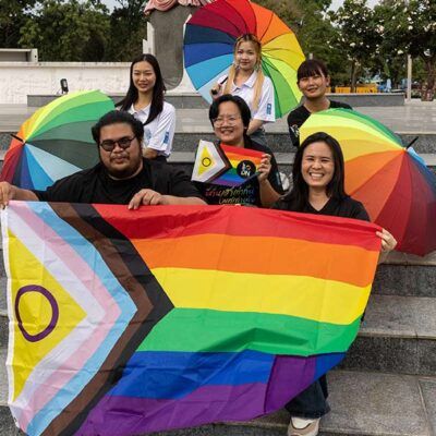six people with rainbow umbrellas and a flag