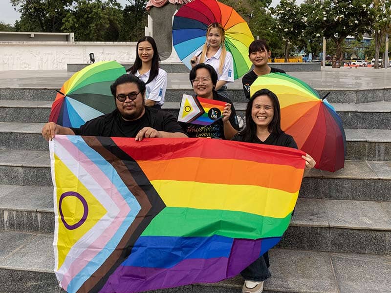 six people with rainbow umbrellas and a flag