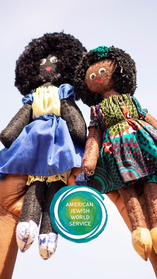 two handmade dolls wearing colorful dresses, being held by two hands in the air