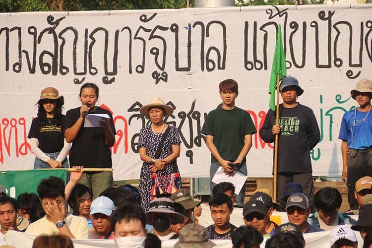 six people standing in front of crowd on stage, with a banner behind them