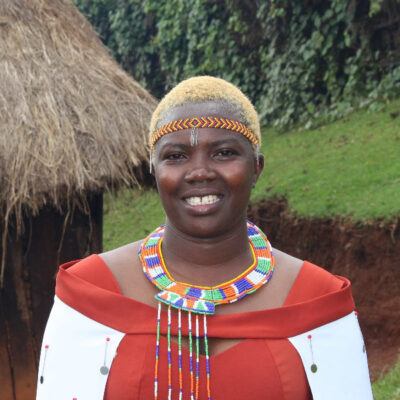 woman wearing red top and beaded accessories behind grass and a straw roof