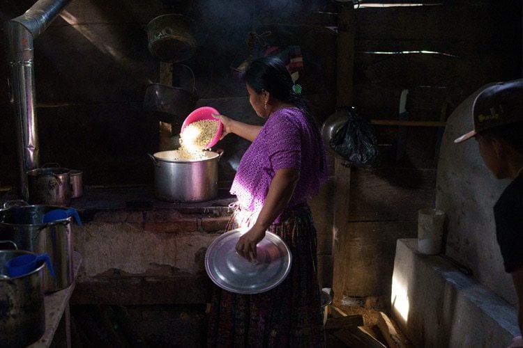 woman in a dark kitchen with light coming through the window, preparing food