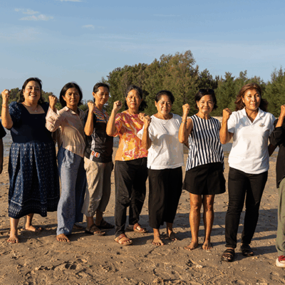 nine women in front of a body of water, raising solidarity fists together