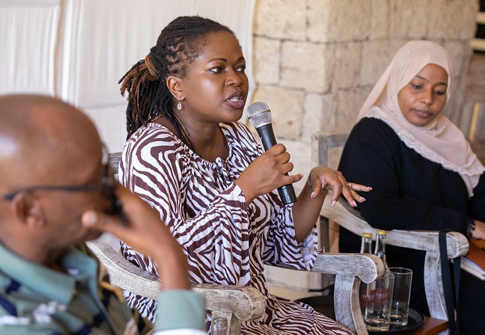 three people seated, one woman in the middle speaking into a microphone