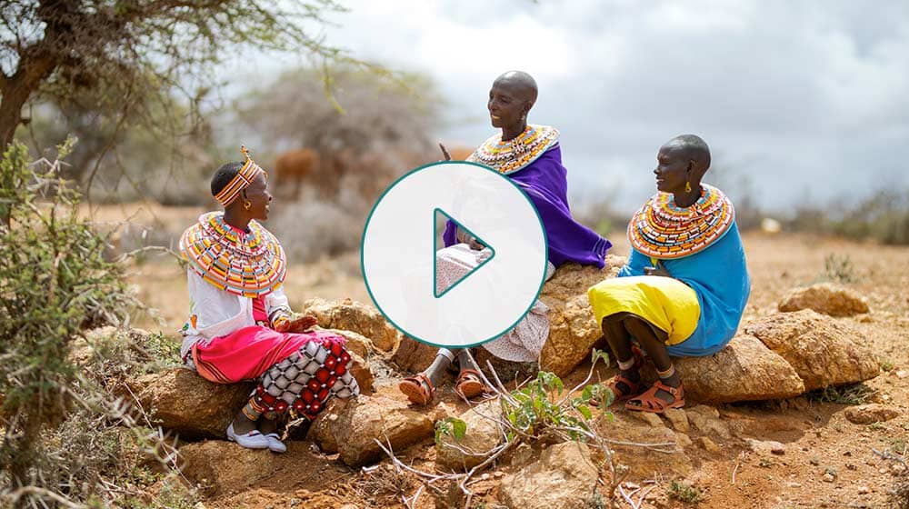 three women sitting outside, with a play button overlaid