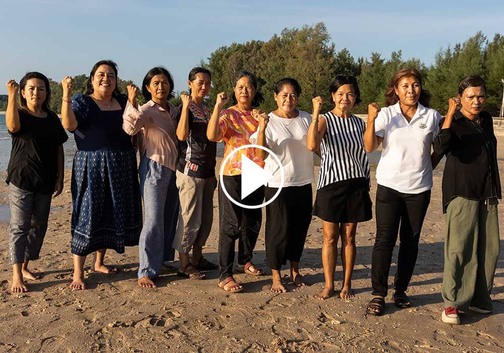 nine women standing on the beach raising solidarity fists