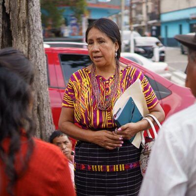 woman speaking to group of people outside, holding folders of papers