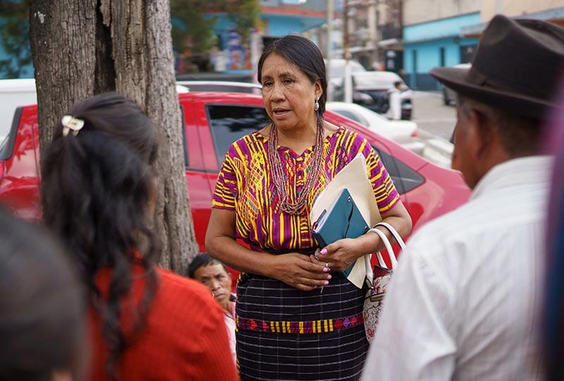 woman speaking to group of people outside, holding folders of papers