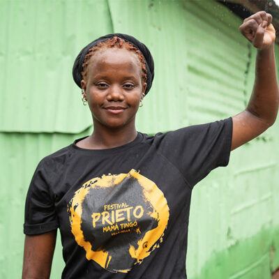 woman in black tshirt in front of green building, raising solidarity fist