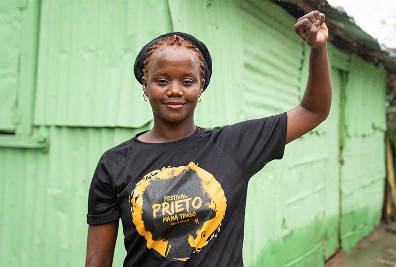 woman in black tshirt in front of green building, raising solidarity fist