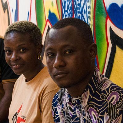 three people smiling at camera in front of a graffitied wall